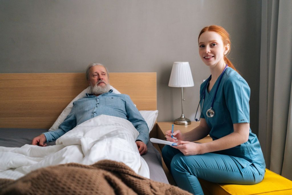 A carer sitting by an older man's bed and writing notes