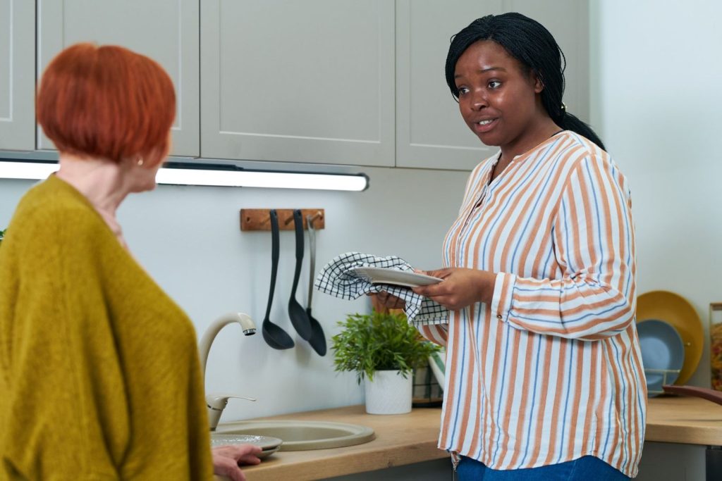 A home help drying a plate and chatting with an older woman in her kitchen