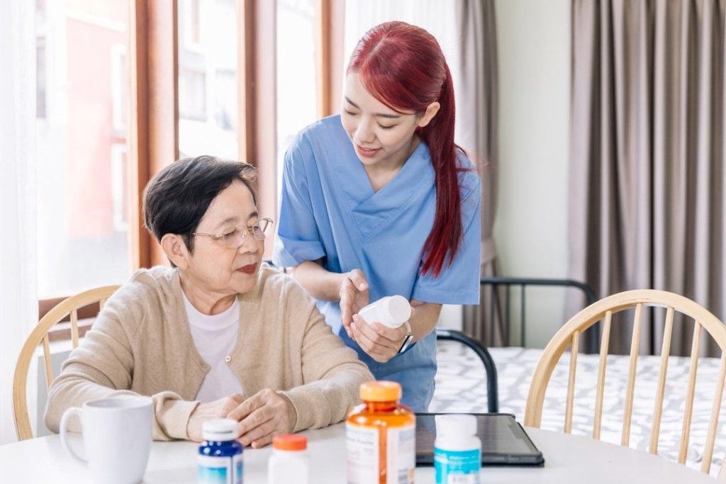 A carer explaining a medicine bottle to an older woman at a kitchen table