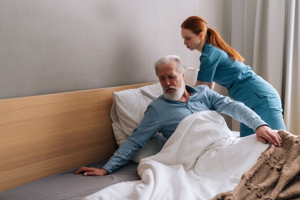 A carer helping an older man sit up and get out of bed