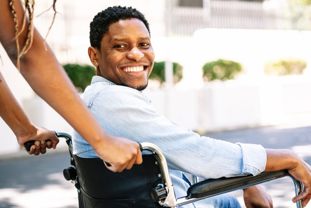 A smiling young man in a wheelchair on an outing with his support worker
